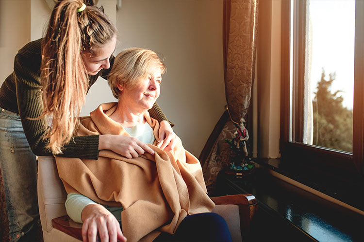 volunteer wrapping a blanket around a hospice patient sitting in a chair